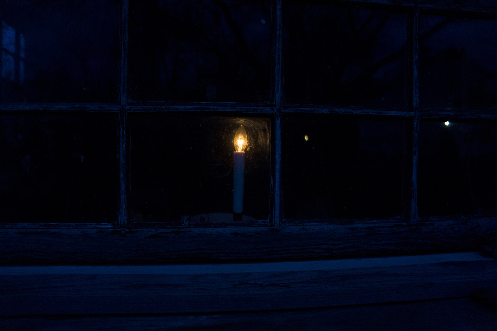 A candle glowing behind a window