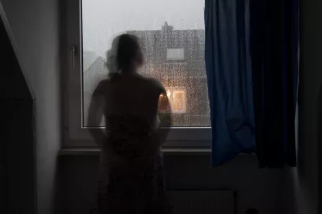 A lady standing in front of the window during a rainy day